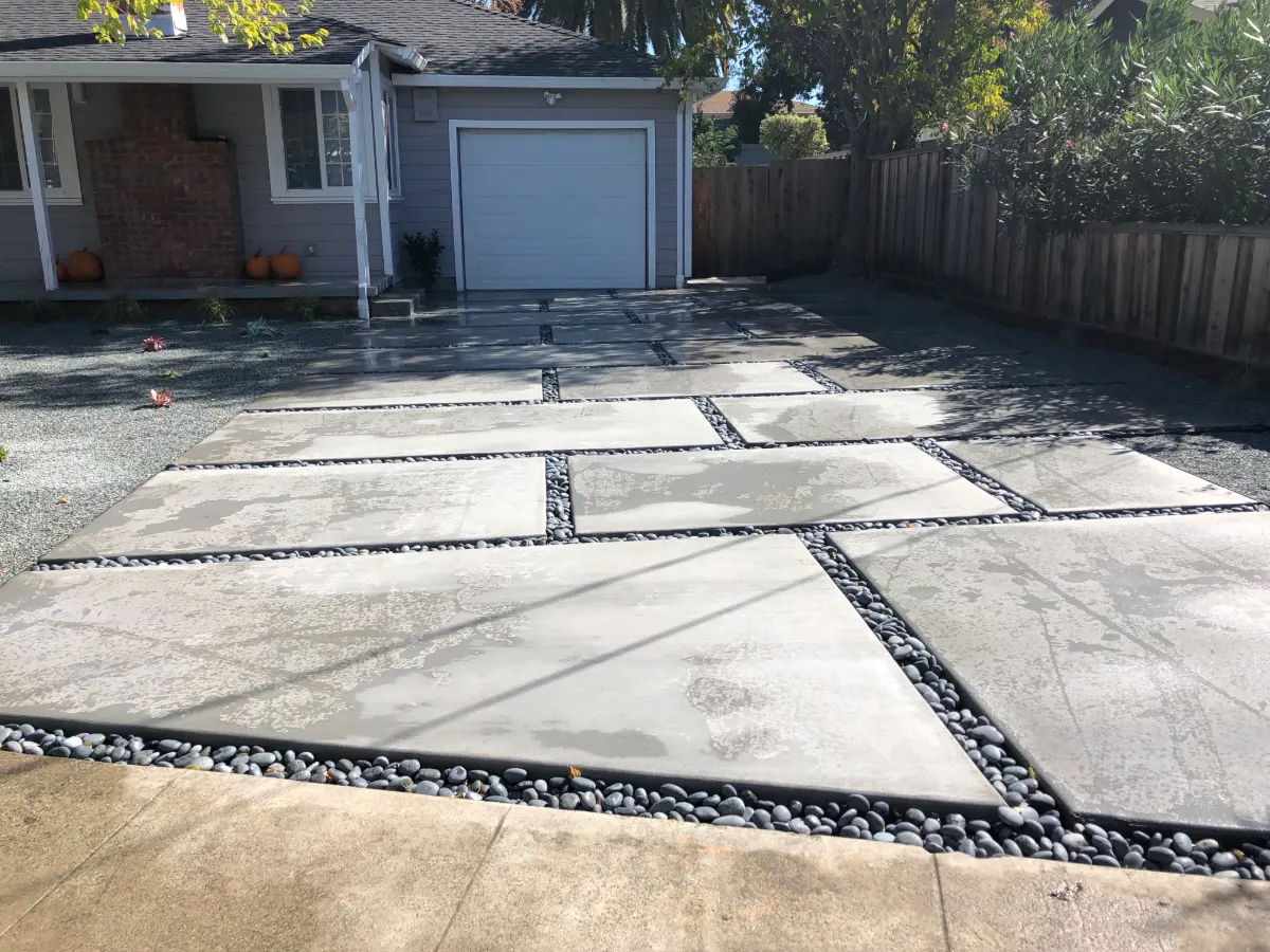 Large-format concrete paver patio with black river rock joints in a backyard