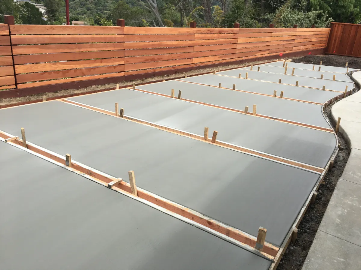 Freshly poured concrete patio slabs in wood forms beside a new redwood fence