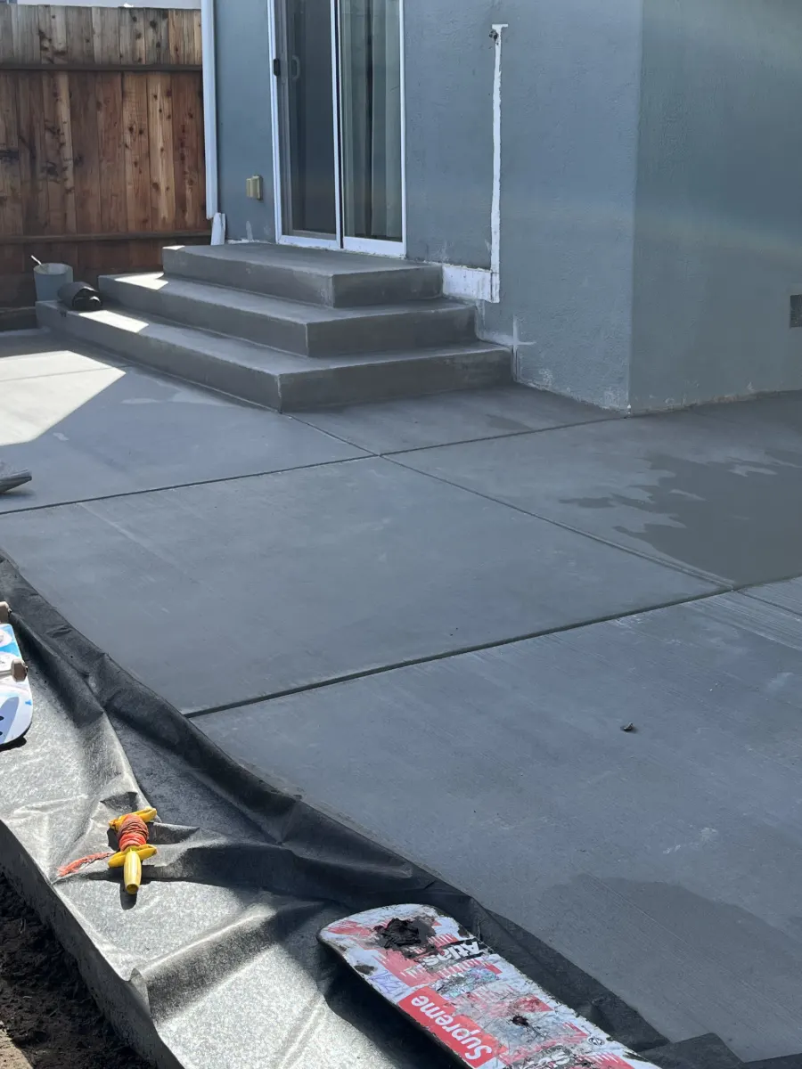 Newly poured concrete patio and entry steps behind a house